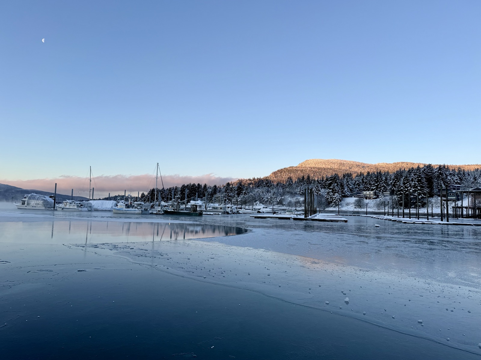 Frozen harbor with fishing boats and snowy hills at dawn